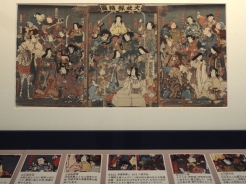 大社縁結図<br>歌川豊国（三代）／江戸時代（1851年）<br>中央下の神様が手を添えるぶ厚い帳面は、結ばれたカップルの名前を記した「縁結人名帳」。神様たちの顔、実は当時の歌舞伎役者の似顔絵になっている。