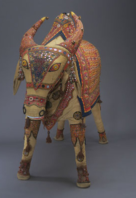 人形［牛］（国：インド）<br>みんぱく所有民族資料<br><br>インドの結婚式の際、輿入れする花嫁の行列の車に載せられる一種のぬいぐるみで、凝った美しい刺繍が施されている。この刺繍は多くの場合、手紡ぎ・手織りの木綿地になされる。グジャラート州で1960年頃製作され、今も使用されている。